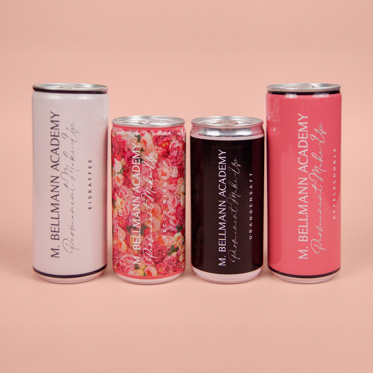 Vier Getränkedosen in unterschiedlichen Designs und Farben im Branding der M. Bellmann Academy, stehend nebeneinander