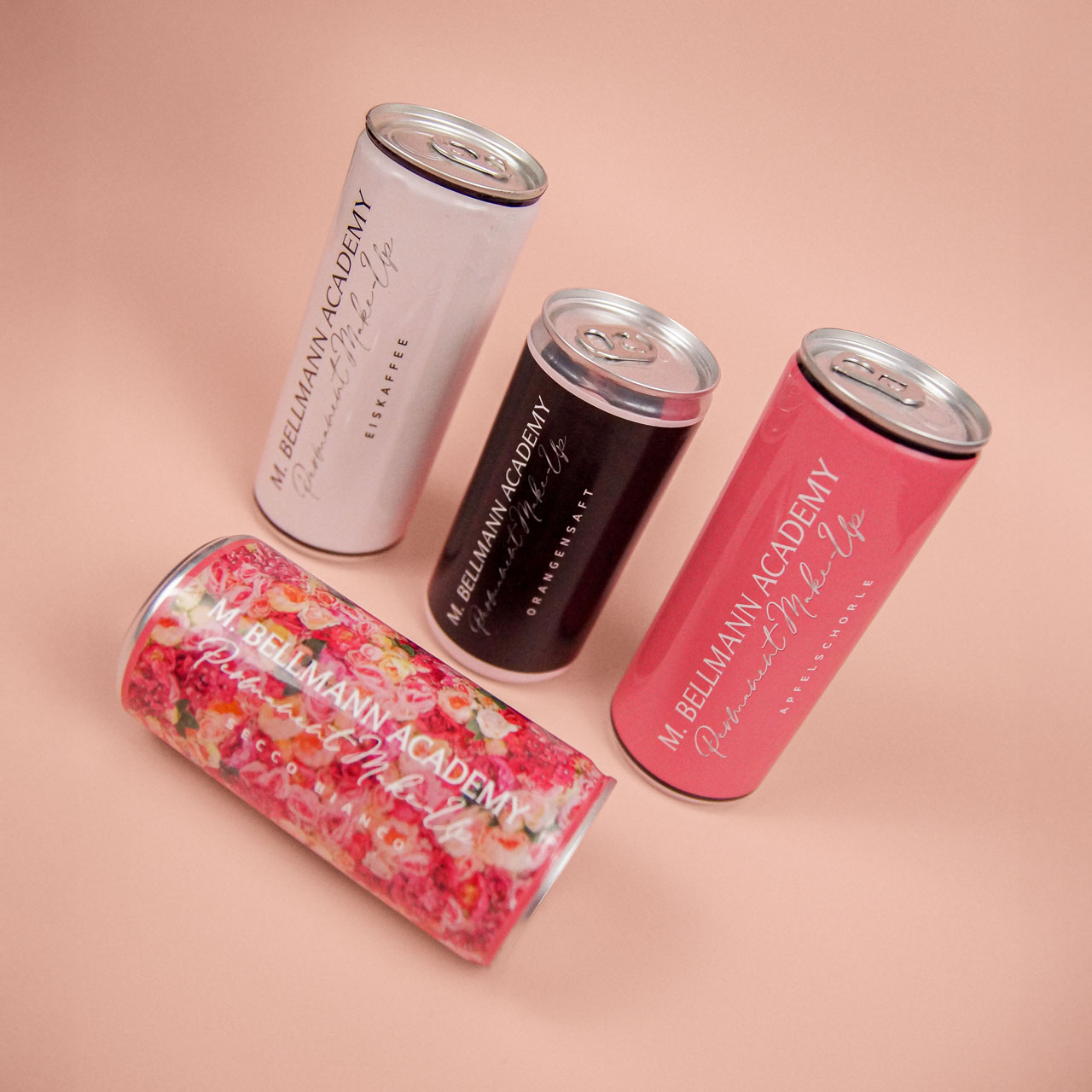 Getränkedosen im Branding der M. Bellmann Academy, stilvoll arrangiert auf roséfarbenem Hintergrund